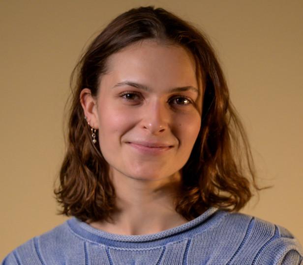 Headshot of Flora Ferguson against a neutral background. She is smiling and wears a lavender knit sweater