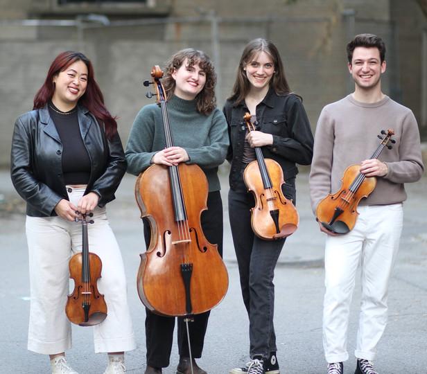 string quartet members standing outside and posing for photo behind a building