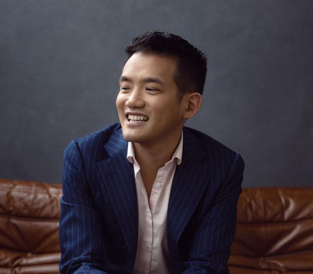 headshot of a man sitting on a couch wearing a striped suit