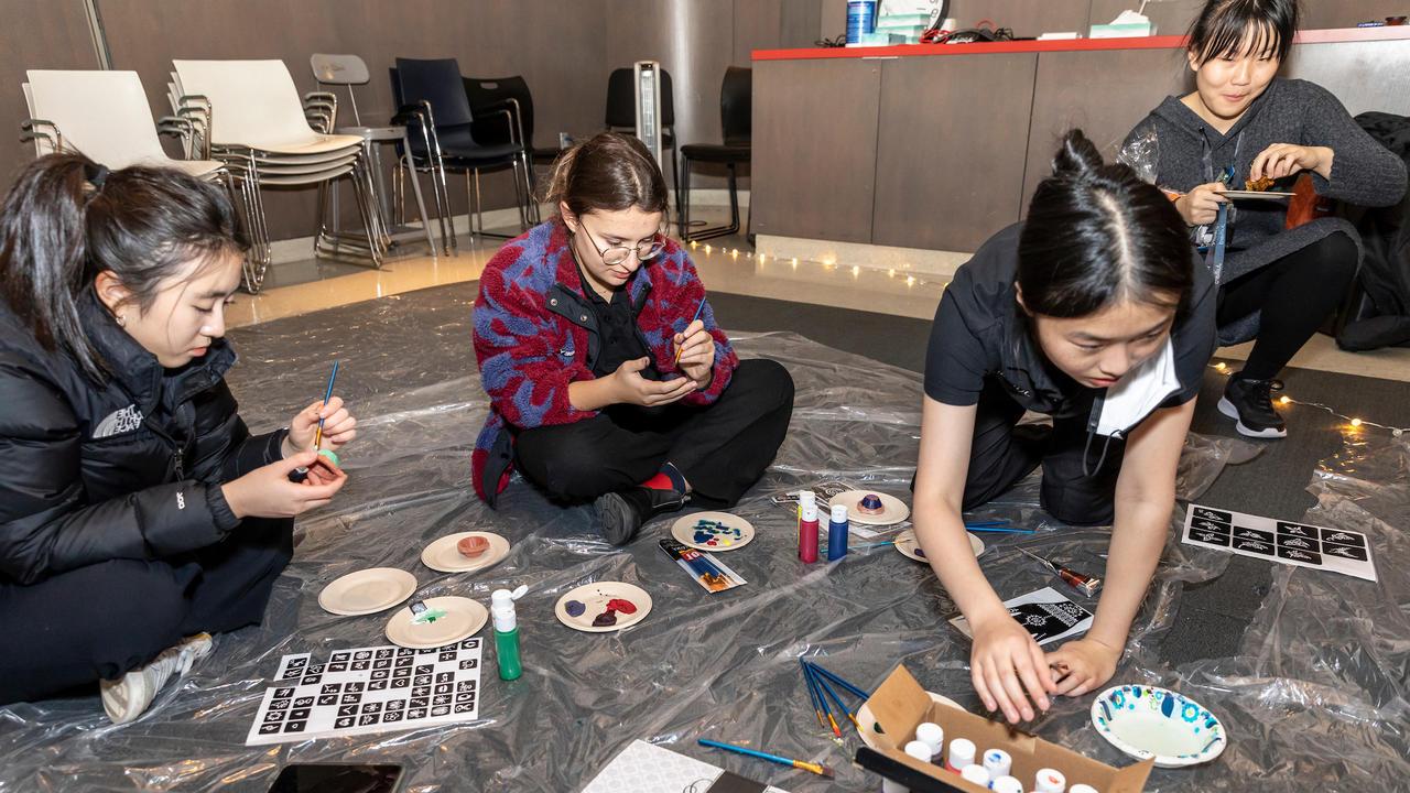 Individuals are sitting on the floor painting individual pieces of artwork