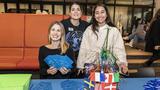 Three people at a welcome table in the lobby distribute paper "passports" for the international festivities