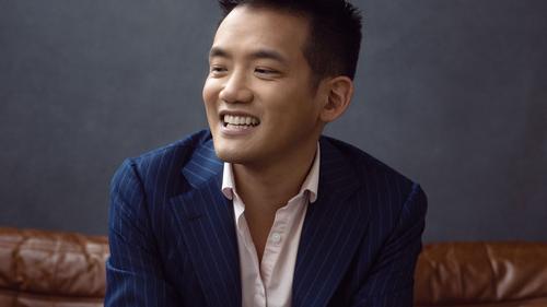 headshot of a man sitting on a couch wearing a striped suit